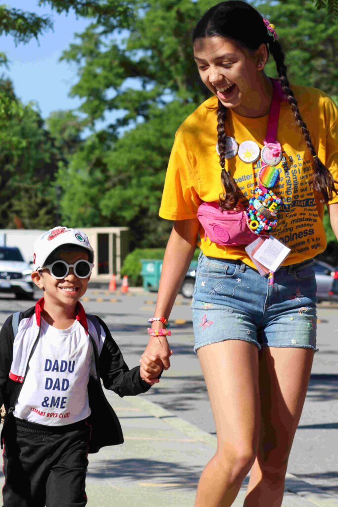 Day Camp in 2025. Counselor walking with little camper. Holding hands.